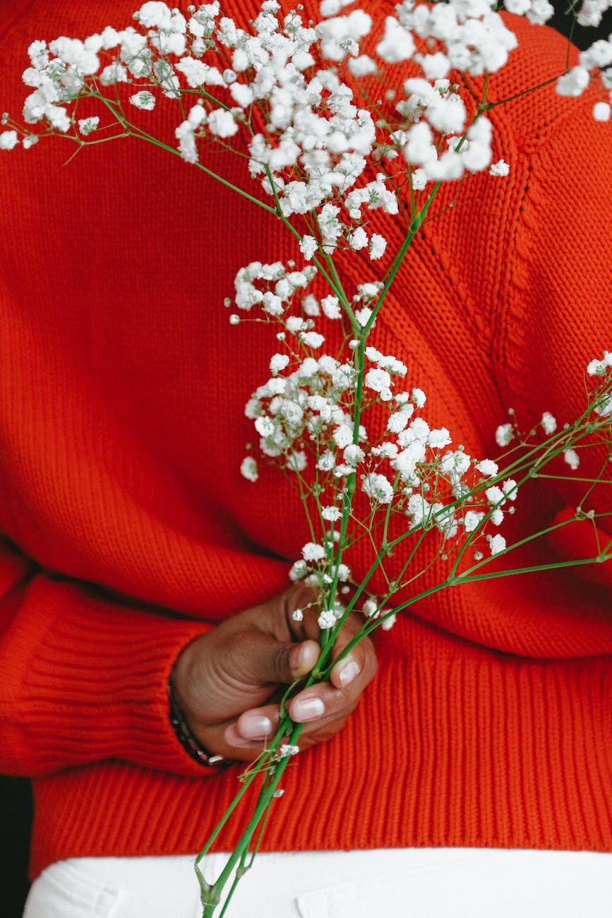 crop black female in bright sweater holding blooming branch
